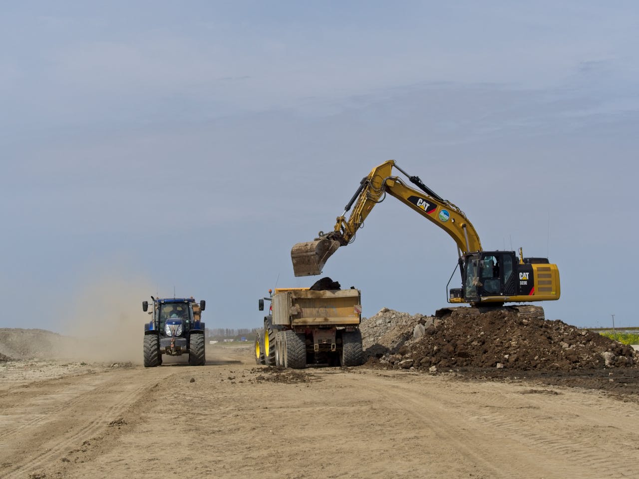 Inicio An excavator loads a dump truck on a dusty construction site in Noord-Holland, Nederland.